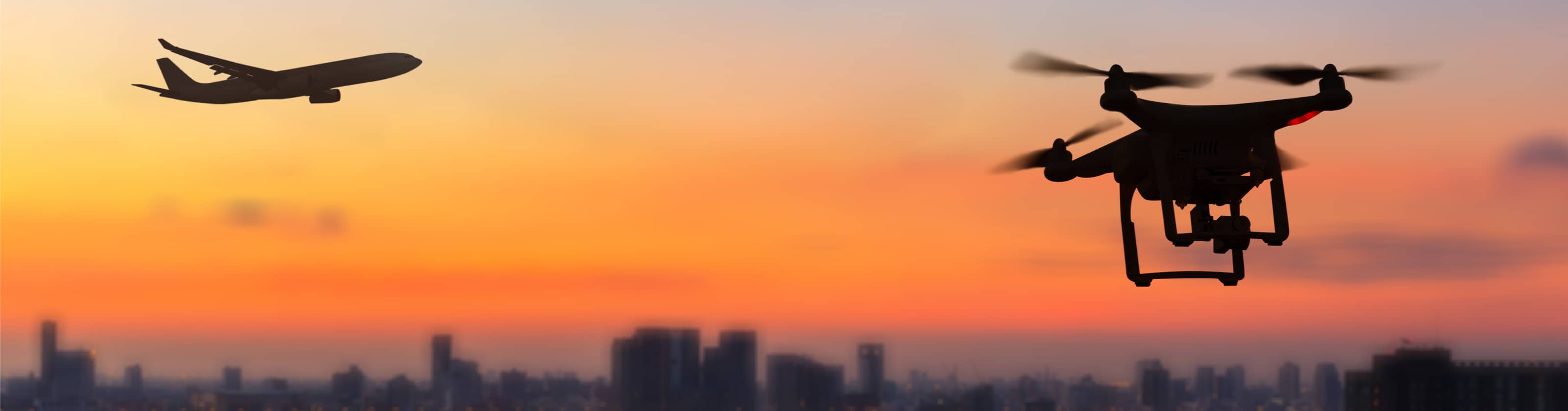 Silhouetted drone approaching a commercial aeroplane at sunset